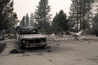 A burned truck sits in the driveway of burned out residential home in the Balboa neighborhood of Spokane, Washington, on August 2, 2026. Fast-moving fires left a trail of destruction in the northwestern US city of Spokane on Sunday, with officials reporting hundreds of structures reduced to cinders. Thousands of people were ordered to evacuate their homes Saturday and overnight into Sunday, as three separate fires broke out in and around the city in the east of Washington state. (Photo by Erick Doxey / AFP)