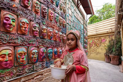 Un&nbsp;infante vestido con un traje tradicional se encuentra junto a un alto relieve de Adel Yazdi, un artista iraní que ha transformado un callejón en uno de los barrios antiguos de Shiraz en una galería de arte permanente al aire libre. (Foto de ATTA KENARE / AFP)
