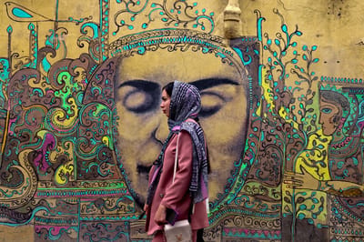 Una mujer pasa junto a un mural pintado por Adel Yazdi, artista iraní que transformó un callejón de uno de los barrios antiguos de Shiraz en una galería de arte permanente al aire libre. (Foto de ATTA KENARE / AFP)