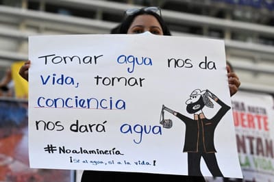A demonstrator holds a placard reading "Drinking Water Gives Us Life, Become Aware Will Give Us Water" during a protest against the reactivation of metallic mining after Congress passed a controversial law in December 2024 in front of the National Library in San Salvador on January 19, 2025. (Photo by Marvin RECINOS / AFP)